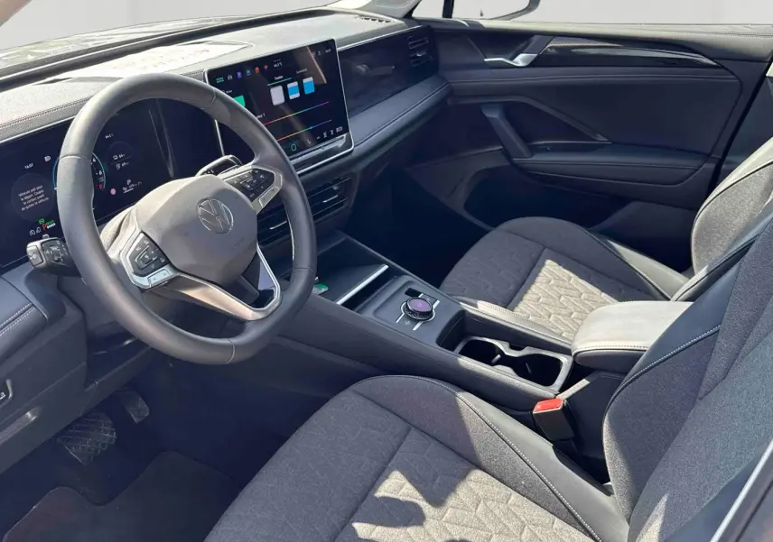 Vue intérieure côté conducteur du Volkswagen Tiguan eHybrid 2025, avec tableau de bord numérique et sièges gris tissu.