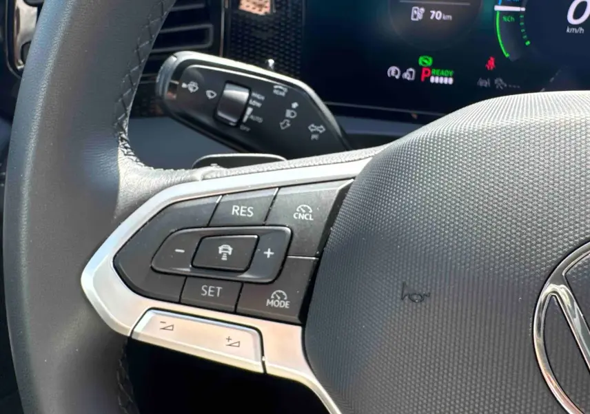 Gros plan sur le volant noir du Volkswagen Tiguan eHybrid 2025, montrant les commandes de régulateur de vitesse à gauche.