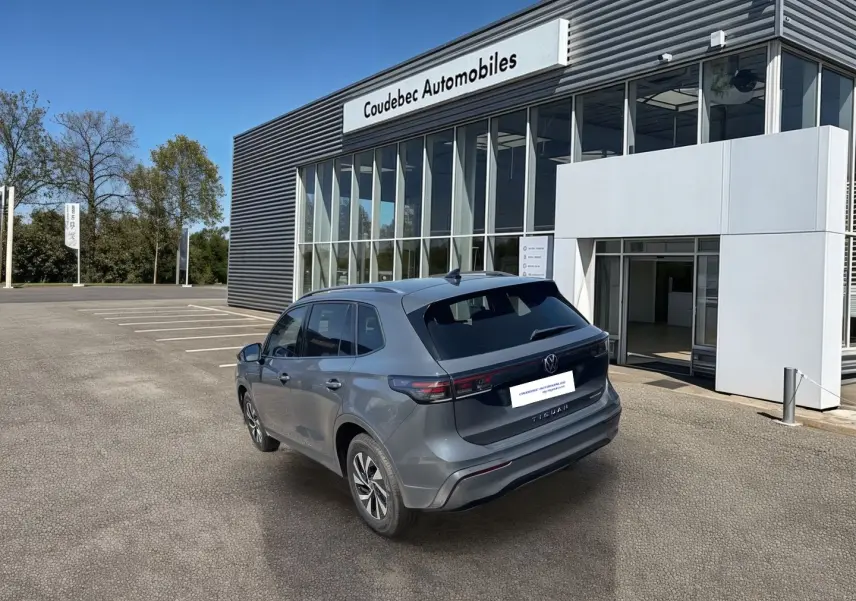 Vue 3/4 arrière du Volkswagen Tiguan gris électrique stationné devant un bâtiment moderne de concession automobile.
