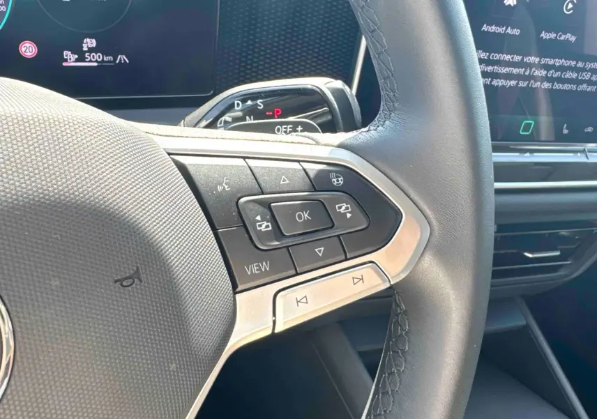 Gros plan sur le volant multifonction noir avec commandes intégrées du Volkswagen Tiguan 2025, affichage numérique en arrière-plan.