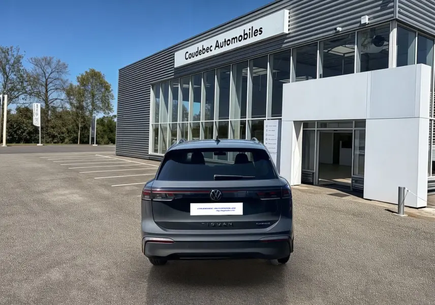 Vue arrière d'un Volkswagen Tiguan eHybrid gris stationné devant un bâtiment moderne de concession automobile.