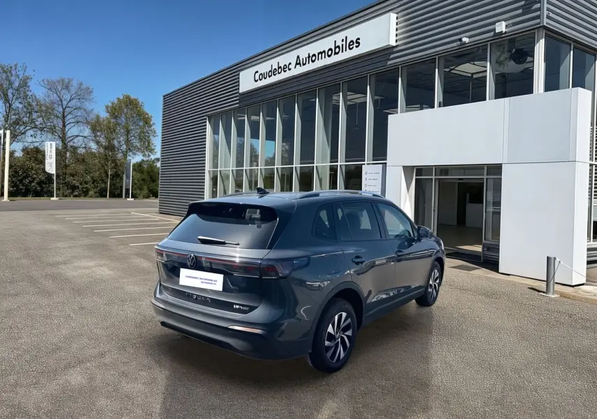 Vue 3/4 arrière droite du Volkswagen Tiguan eHybrid gris devant un bâtiment de concession Coudebec Automobiles.