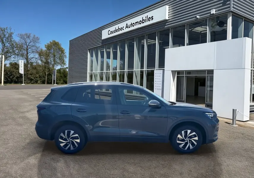 Vue latérale droite du Volkswagen Tiguan eHybrid gris devant un showroom Coudebec Automobiles, avec jantes alliage distinctives.