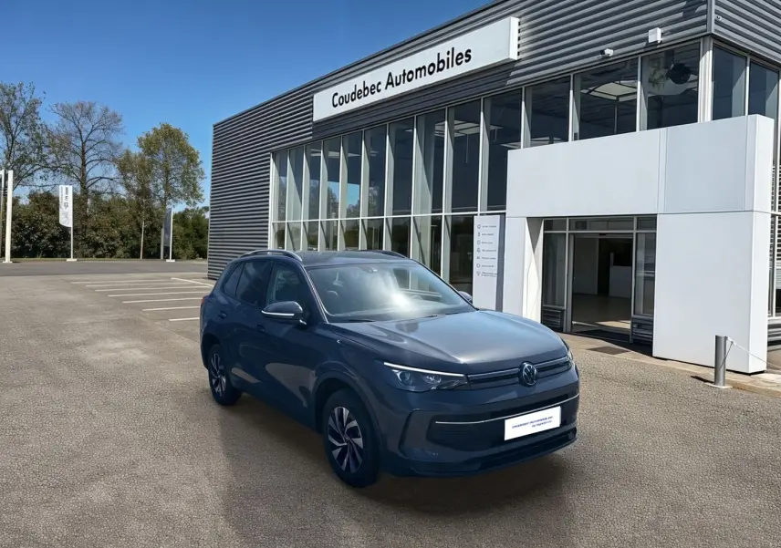 Vue 3/4 avant d'un Volkswagen Tiguan 1.5 eHybrid gris stationné devant un concessionnaire Coudebec Automobiles.