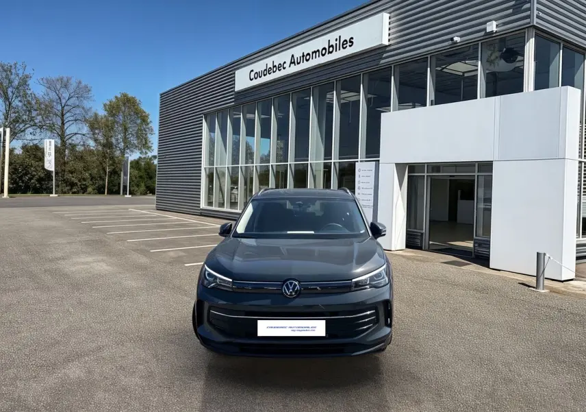 Vue avant d'un Volkswagen Tiguan 1.5 eHybrid gris stationné devant un bâtiment moderne de concession automobile.