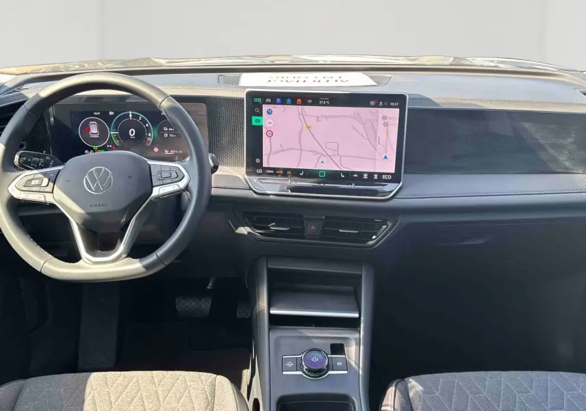 Vue intérieure frontale du tableau de bord du Volkswagen Tiguan 2025 avec écran tactile central et volant multifonction noir.
