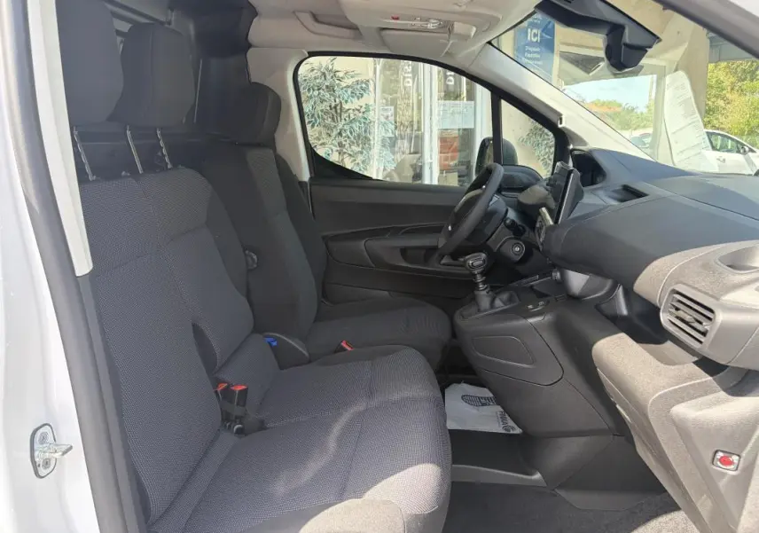 Vue intérieure côté conducteur du Peugeot Partner blanc 2026, montrant les sièges tissu, volant multifonctions et tableau de bord.