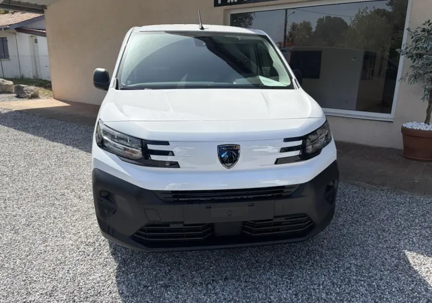 Vue de face d’un Peugeot Partner blanc 2026 avec pare-chocs noir et logo Peugeot central bien visible.