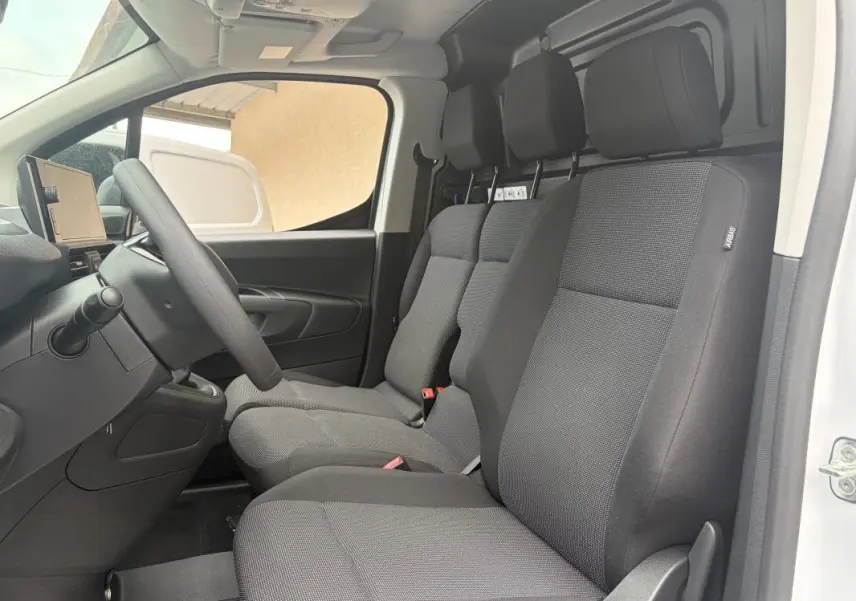 Vue intérieure côté conducteur du Peugeot Partner blanc 2026, montrant les sièges tissu gris et le volant multifonctions.
