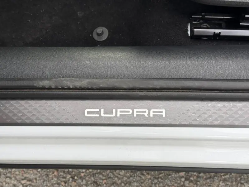 Gros plan sur la plaque de seuil de porte avec logo CUPRA, sur le côté gauche d’un CUPRA Formentor blanc Nevada métallisé.