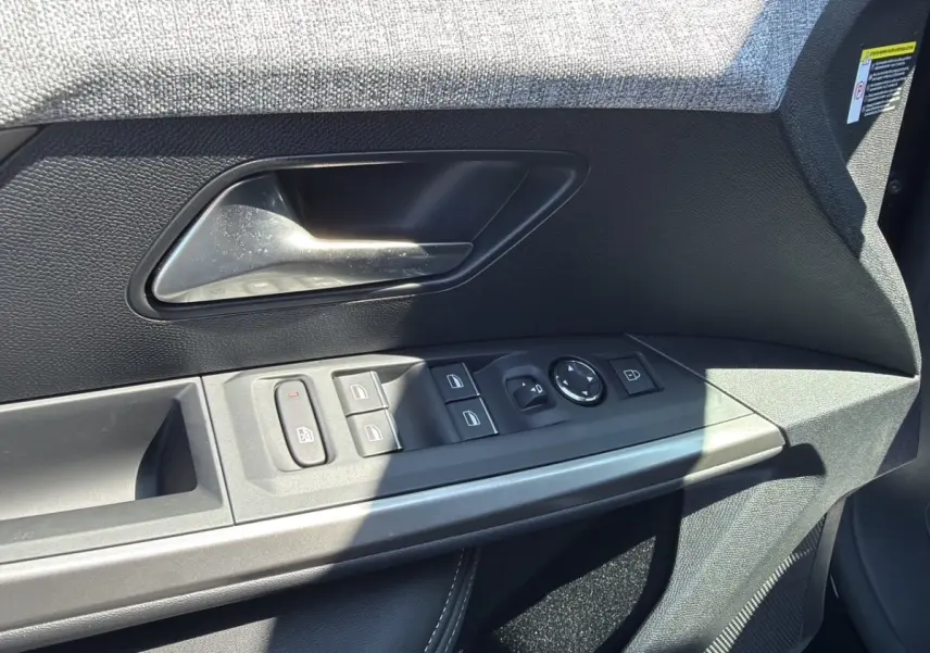 Gros plan sur la porte avant gauche noire du Peugeot 5008 2025, avec commandes électriques des vitres et poignée intérieure.