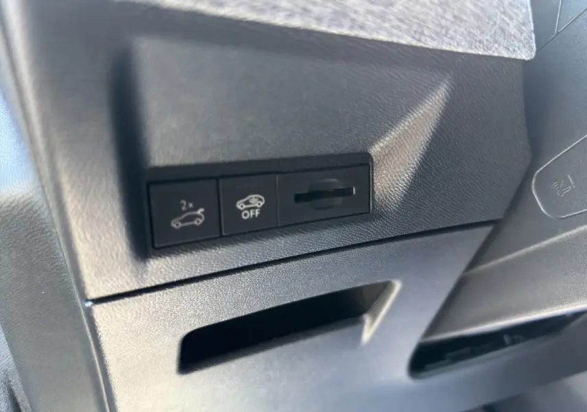 Détail des commandes d'ouverture du coffre et désactivation d'assistance sur tableau de bord noir intérieur Peugeot 5008 hybride.