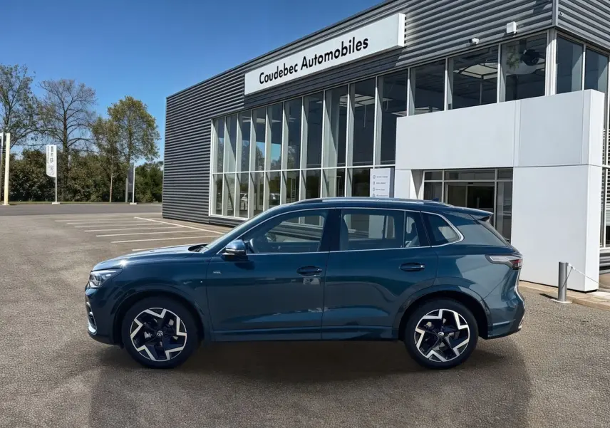 Vue latérale droite du Volkswagen Tiguan 2025 bleu, avec jantes alliage 19 pouces et finition R-Line devant un concessionnaire.