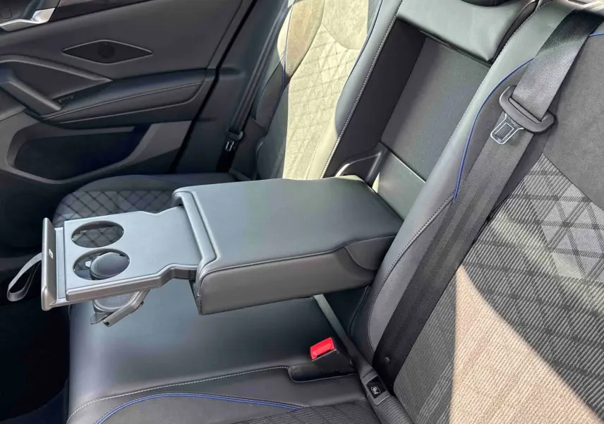 Vue intérieure arrière côté droit du Volkswagen Tiguan 2025, sièges noirs avec surpiqûres bleues et accoudoir central avec porte-gobelets.