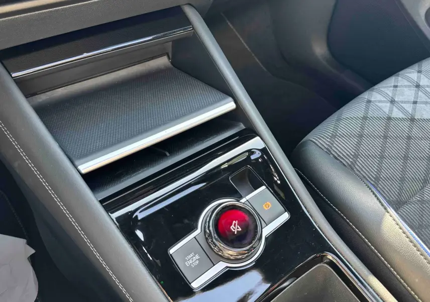 Gros plan sur la console centrale noire brillante du Volkswagen Tiguan 2025 avec bouton rotatif et siège tissu gris à motifs.