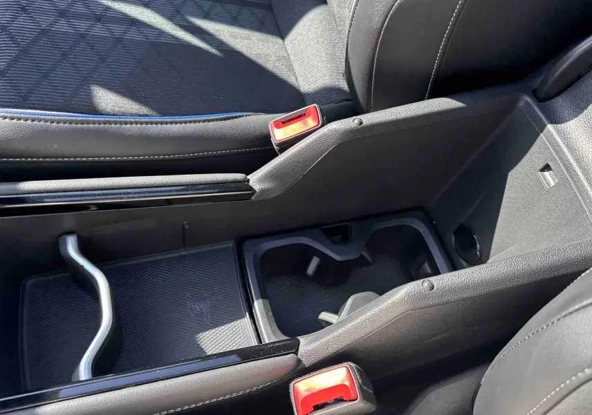 Gros plan sur la console centrale noire du Volkswagen Tiguan 2025, montrant les porte-gobelets et le rangement intérieur.