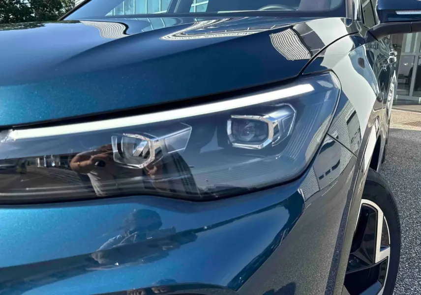 Gros plan sur le phare avant droit et la jante alliage 19 pouces du Volkswagen Tiguan bleu 2025.