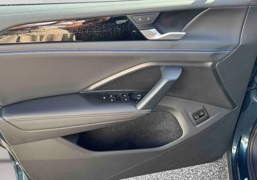 Vue rapprochée de la porte avant gauche du Volkswagen Tiguan 2025 bleu, avec garniture noire et surpiqûres bleues.