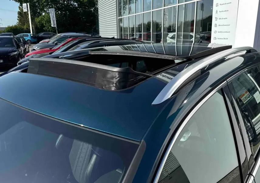 Vue 3/4 arrière droite du Volkswagen Tiguan bleu 2025 avec toit ouvrant panoramique et barres de toit argentées.