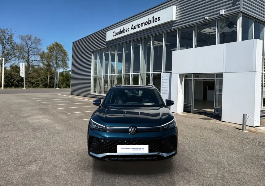Vue de face du Volkswagen Tiguan 2025 bleu, avec calandre noire et phares LED, devant un showroom Coudebec Automobiles.