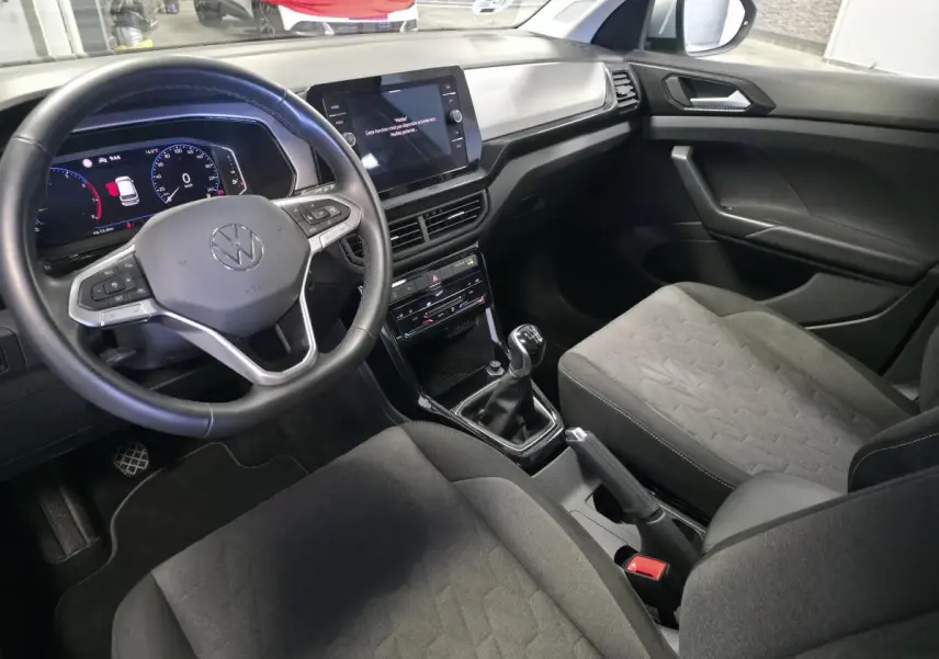Vue intérieure côté conducteur du Volkswagen T-Cross 2025 avec volant cuir, tableau de bord digital et sellerie tissu gris.