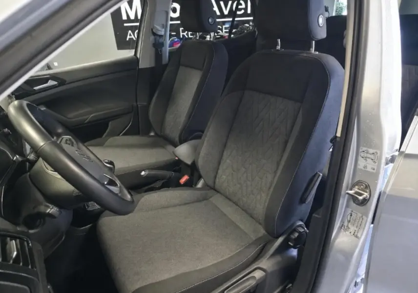 Vue intérieure côté conducteur du Volkswagen T-Cross gris 2025, montrant les sièges avant en tissu et le volant multifonction en cuir.