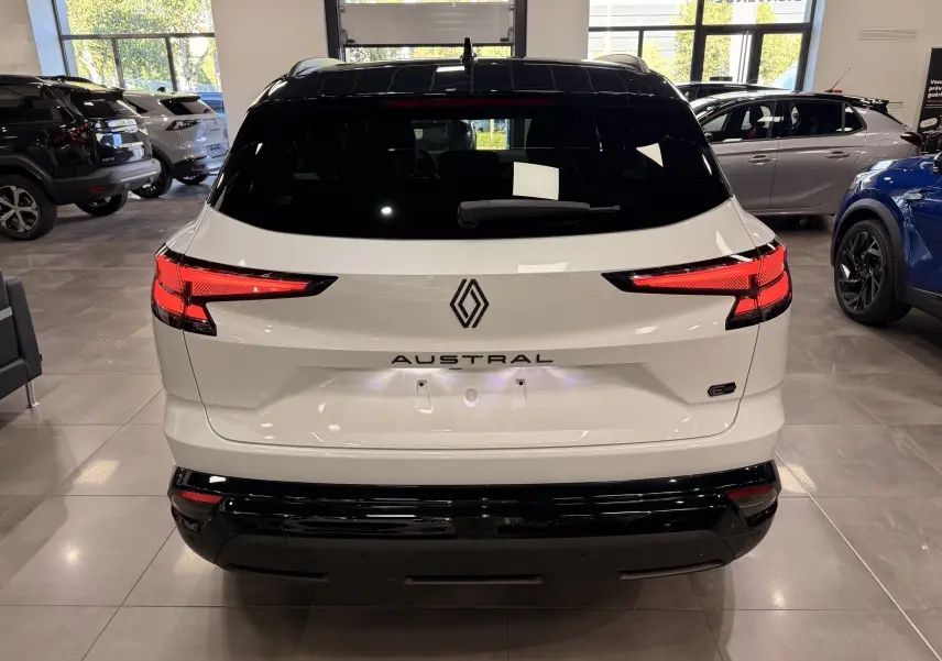 Vue arrière d’un Renault Austral blanc nacré avec toit noir, feux LED allumés dans un showroom lumineux.