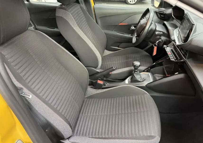 Intérieur de la Peugeot 208 essence jaune clair, vue côté gauche montrant sièges tissu gris et tableau de bord moderne.