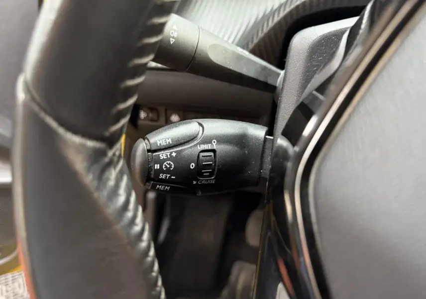 Gros plan sur la commande de régulateur de vitesse derrière le volant d'une Peugeot 208 essence jaune clair.