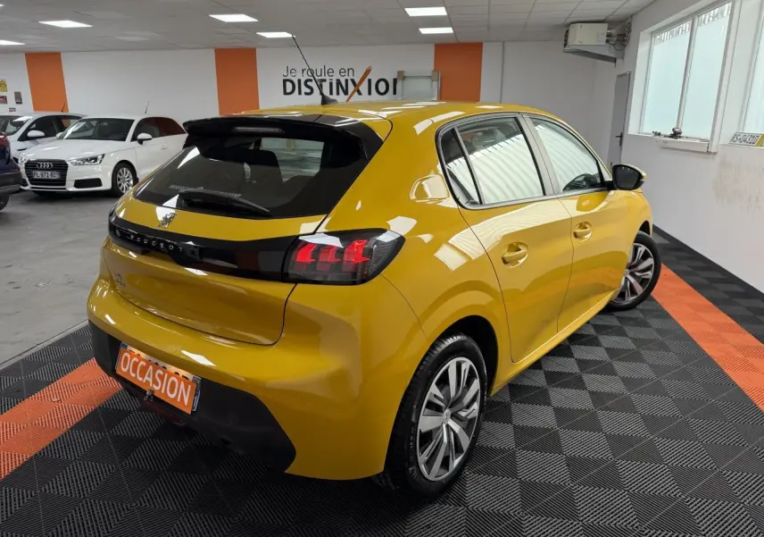 Peugeot 208 jaune clair vue 3/4 arrière droit en intérieur avec jantes 16 pouces et plaque occasion.