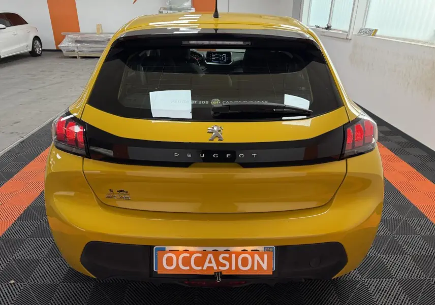Vue arrière d'une Peugeot 208 jaune clair avec bande noire et plaque d'immatriculation orange "OCCASION" en intérieur showroom.