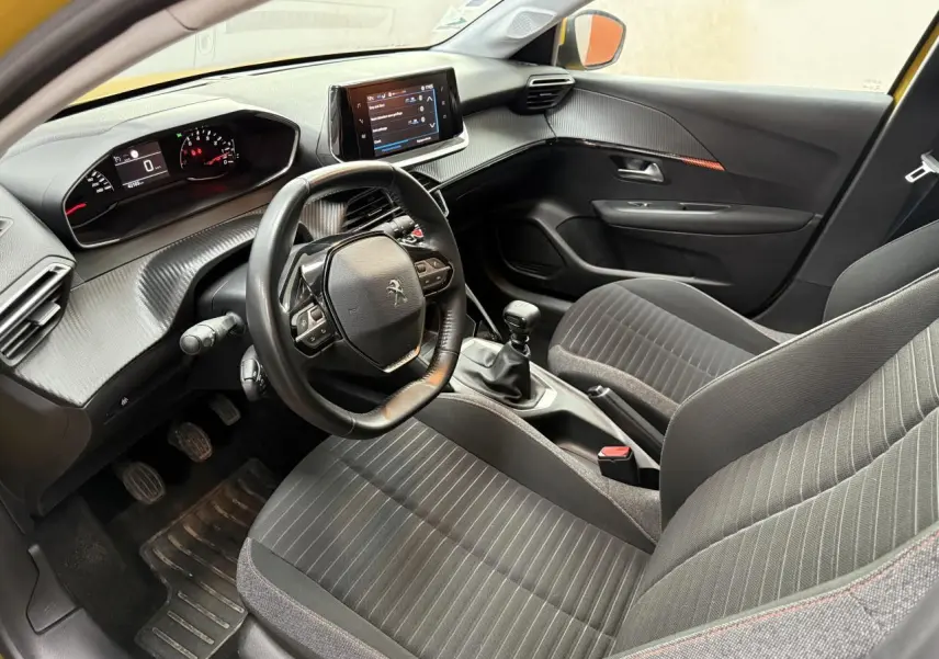 Intérieur avant droit de la Peugeot 208 jaune clair 2020, volant compact, écran tactile et boîte manuelle visibles.