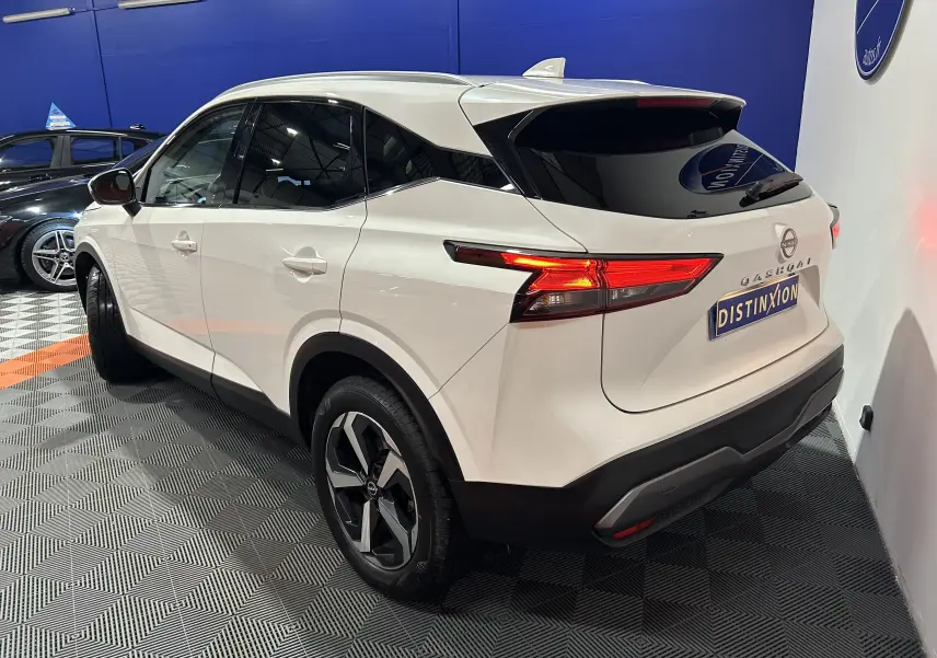Vue 3/4 arrière droite du Nissan Qashqai blanc lunaire avec feux LED allumés et toit panoramique visible.