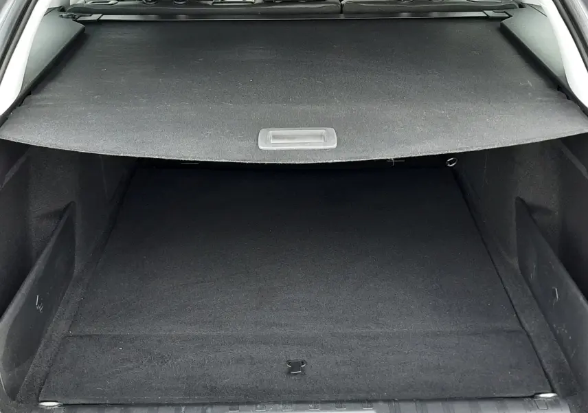 Vue arrière du coffre spacieux et propre de la Peugeot 308 SW gris Artense, avec cache-bagages déployé et intérieur noir visible.