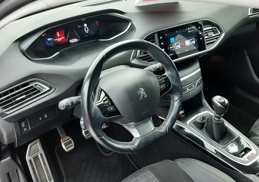 Vue intérieure centrée sur le volant Peugeot et le tableau de bord numérique avec écran tactile, sellerie tissu noir visible.