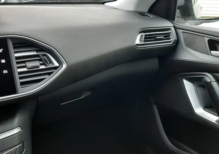 Vue intérieure côté passager de la Peugeot 308 SW 2021 gris Artense, avec tableau de bord et aérateurs noirs.