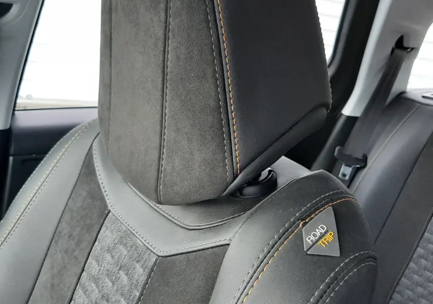 Gros plan sur l'appui-tête et le siège avant droit en tissu noir avec surpiqûres orange et logo Road Trip visible.
