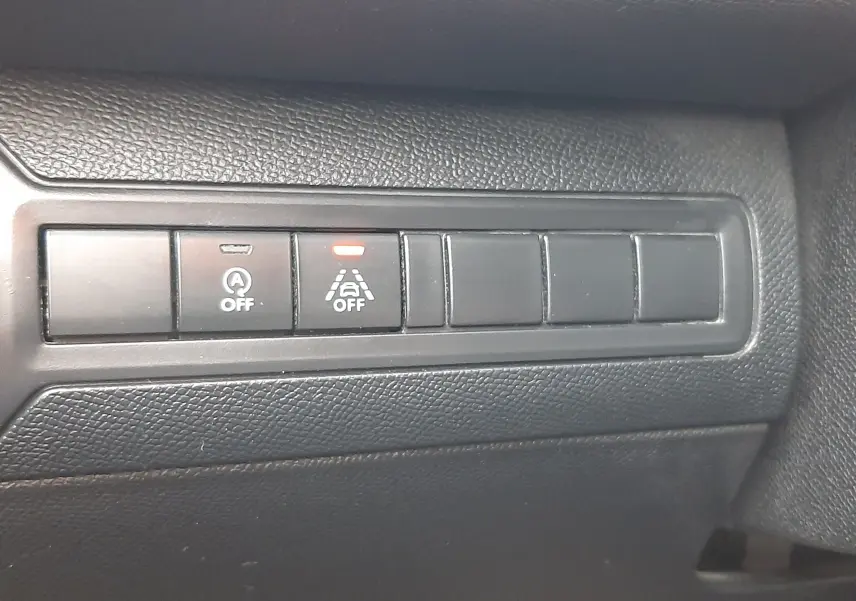 Gros plan sur les boutons de commande noirs du tableau de bord intérieur de la Peugeot 308 SW gris Artense, avec témoin lumineux orange allumé.