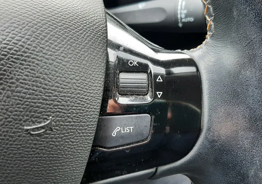 Gros plan sur les commandes à droite du volant en cuir noir avec surpiqûres orange du Peugeot 308 SW gris Artense 2021.