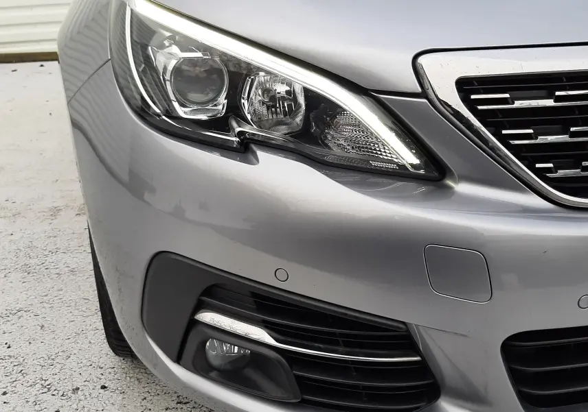 Gros plan sur l'avant droit gris Artense de la Peugeot 308 SW 2021, mettant en valeur le phare LED et la calandre.