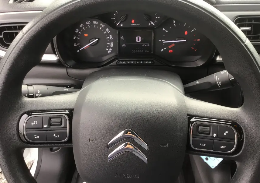 Vue intérieure centrée sur le volant noir de la Citroën C3 Société 2020, avec commandes intégrées et tableau de bord digital.