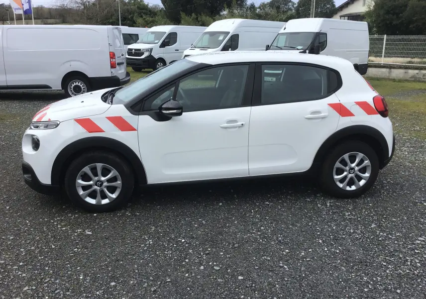 Vue de profil côté gauche d'une Citroën C3 Société blanche avec bandes rouges diagonales sur l'aile avant et arrière.