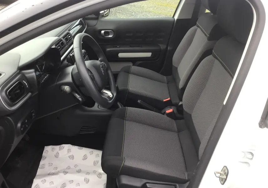 Vue intérieure côté conducteur de la Citroën C3 Société blanche 2020, montrant les sièges avant gris avec surpiqûres vertes et le tableau de bord.
