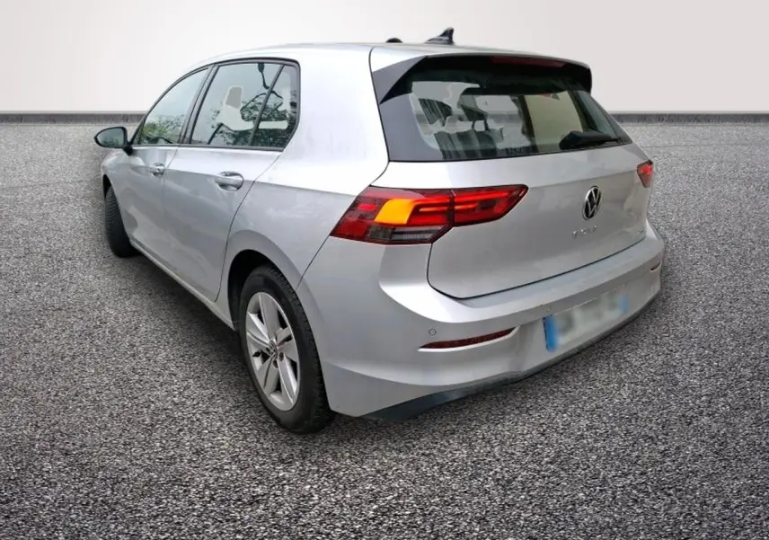 Volkswagen Golf gris clair vue 3/4 arrière droit, feux arrière allumés et jantes alliage visibles.