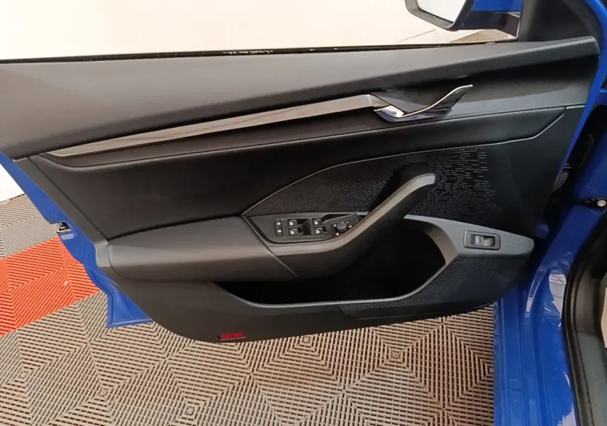 Vue intérieure côté gauche de la porte avant bleue d'une Skoda Octavia 2024 avec commandes électriques et garniture noire.