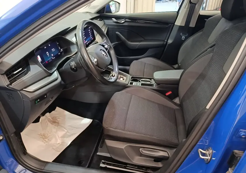 Vue intérieure côté conducteur de la Skoda Octavia 2024 bleue, avec sièges tissu gris et tableau de bord numérique.
