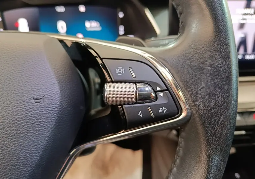 Gros plan sur le volant en cuir noir de la Skoda Octavia 2024, avec commandes multifonctions et molette métallique.