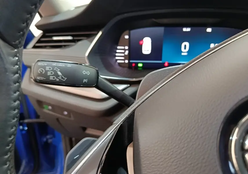 Gros plan sur la commande de régulateur de vitesse à gauche du volant dans l'habitacle bleu d'une Skoda Octavia 2024.
