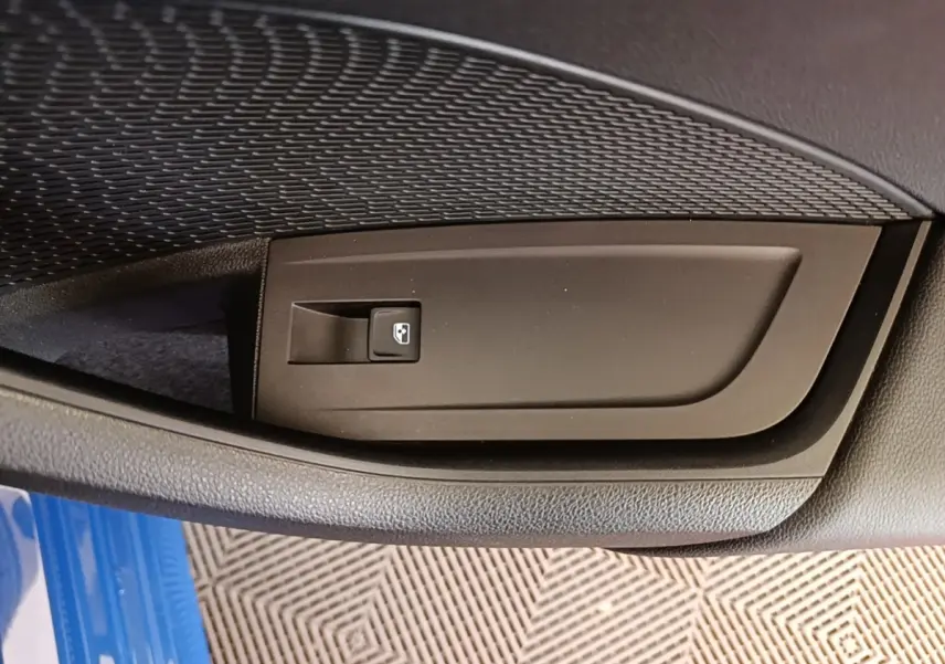 Détail de la commande de lève-vitre sur la porte côté conducteur d’une Skoda Octavia 2024 bleu visible en bas.