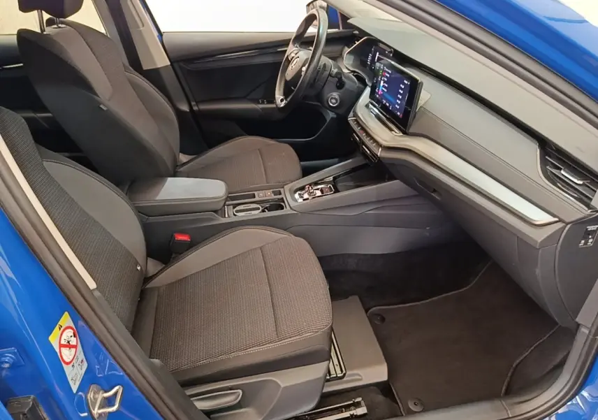 Intérieur avant droit d'une Skoda Octavia 2024 bleu, sièges tissu gris et tableau de bord avec écran tactile.